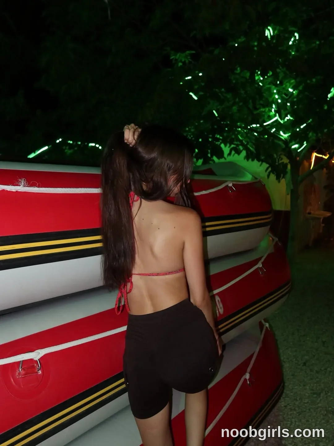 Maria Standing with her back toward the camera beside the stacked boats wearing Red string bikini top in area in Alanya