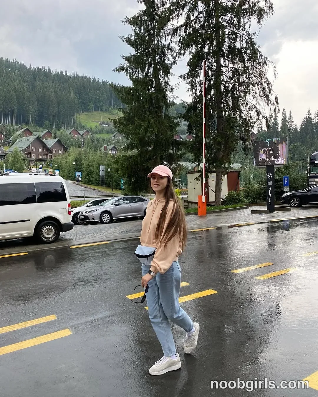 TAANNI Stepping across the road with one foot lifted wearing Pale pink baseball cap