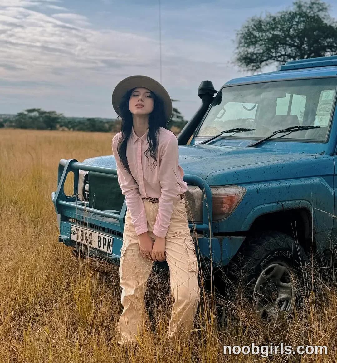 TAANNI standing in front of the vehicle with legs apart wearing pink long-sleeved collared button-front shirt