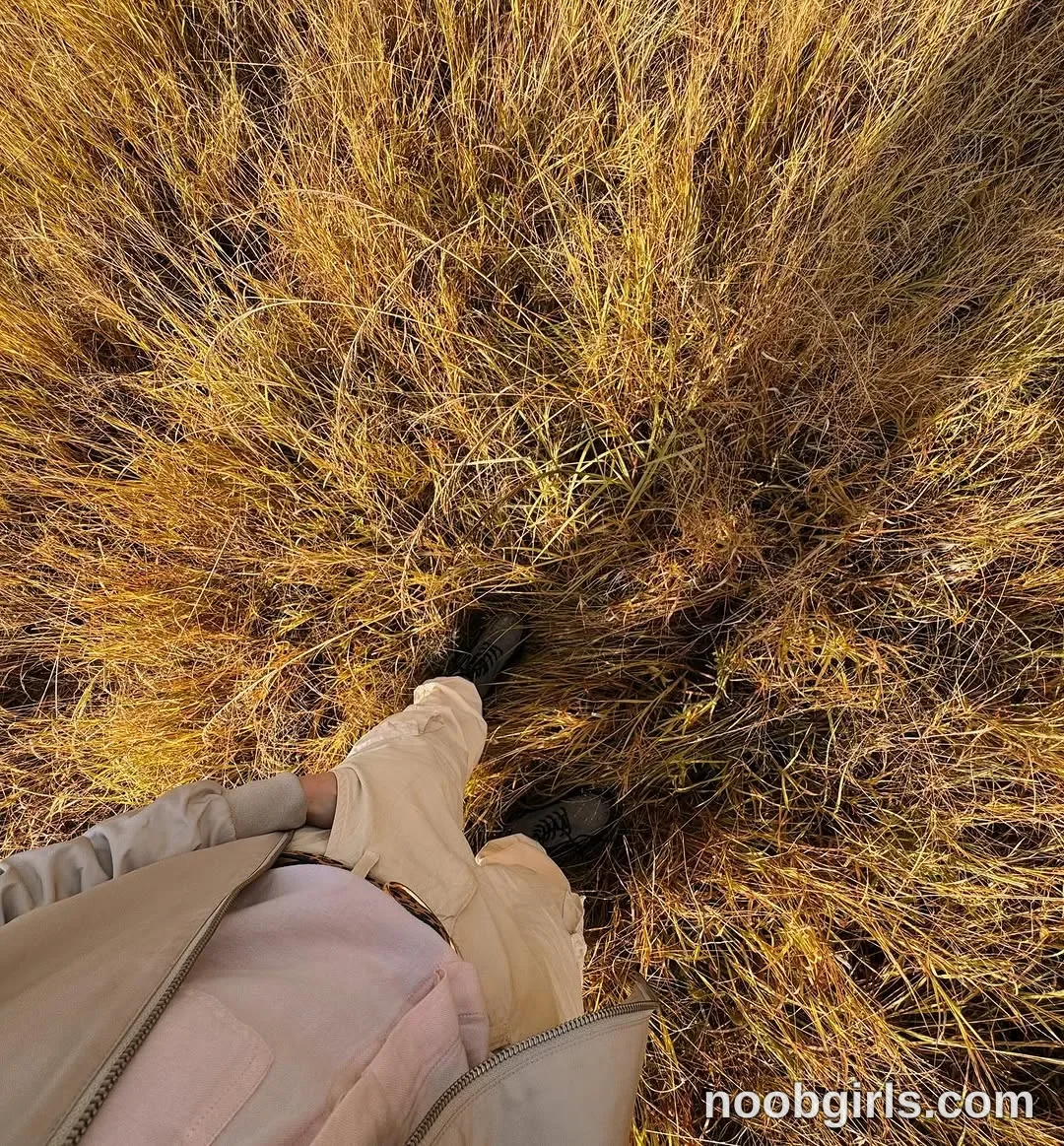 TAANNI Standing among tall grass with one hand in a trouser pocket wearing Light beige zip-front jacket