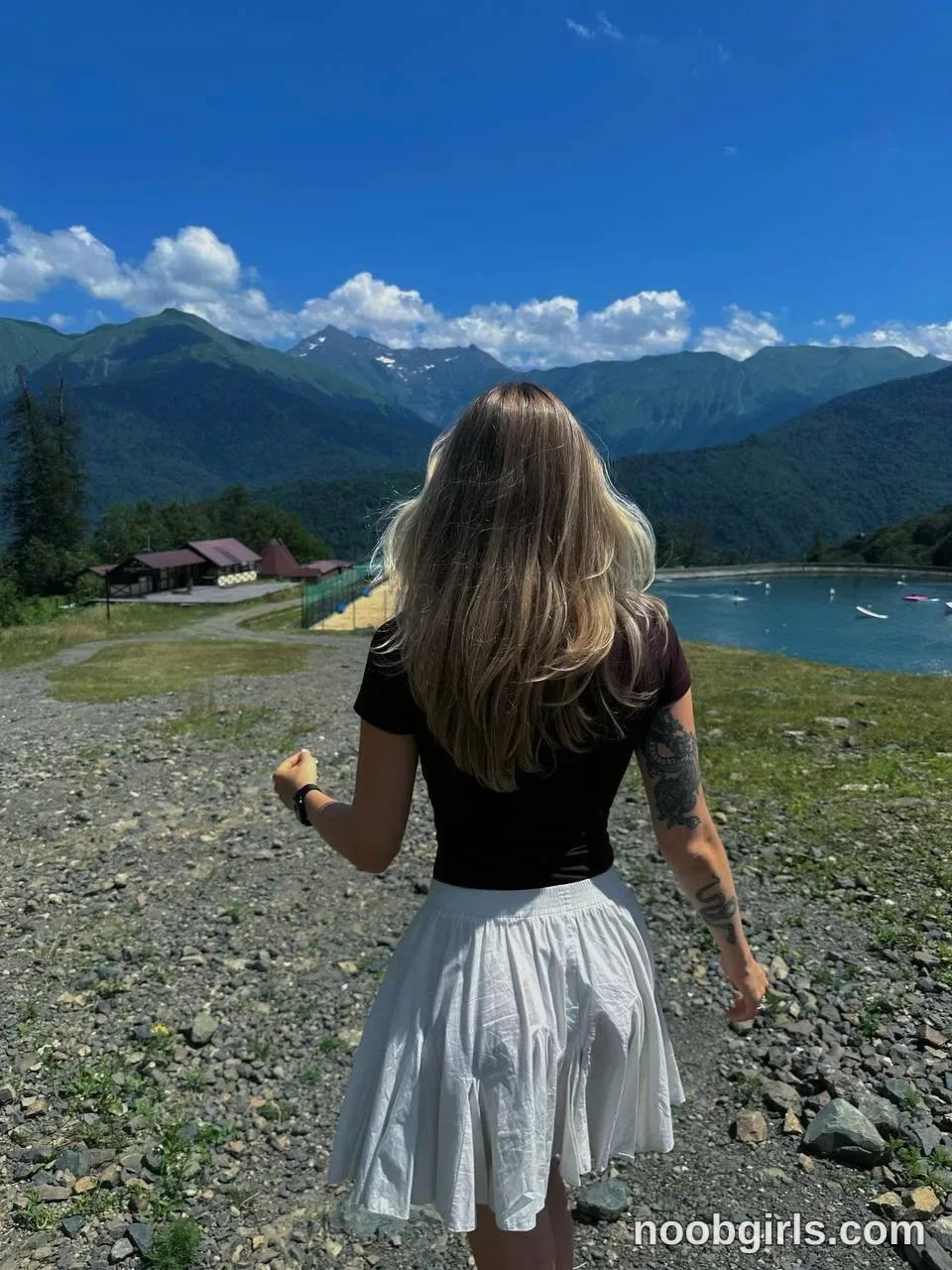 tastypoint walking away from the camera on a gravel path towards a lake wearing short-sleeved black or dark brown t-shirt