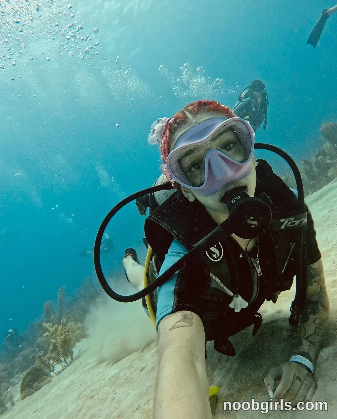 Alicia scuba diving near the seabed with one arm extended toward the camera wearing black and turquoise short-sleeved wetsuit