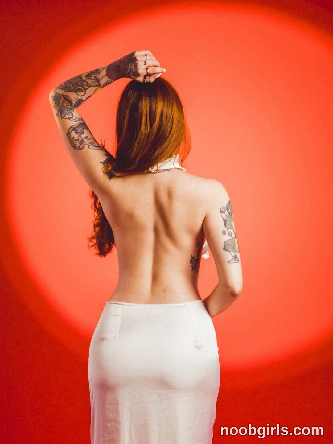Alicia Standing with her back toward the camera wearing White backless garment with a neck strap and a long skirt