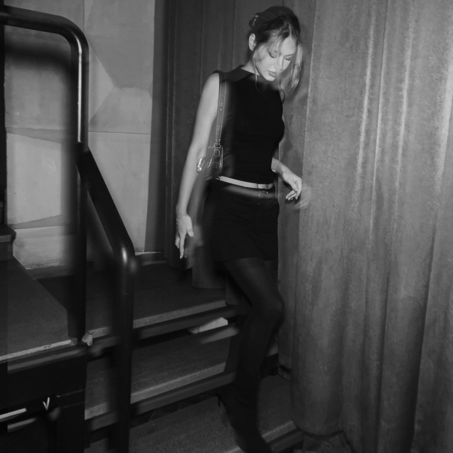 tollysage walking down stairs wearing black sleeveless top in staircase next to curtain