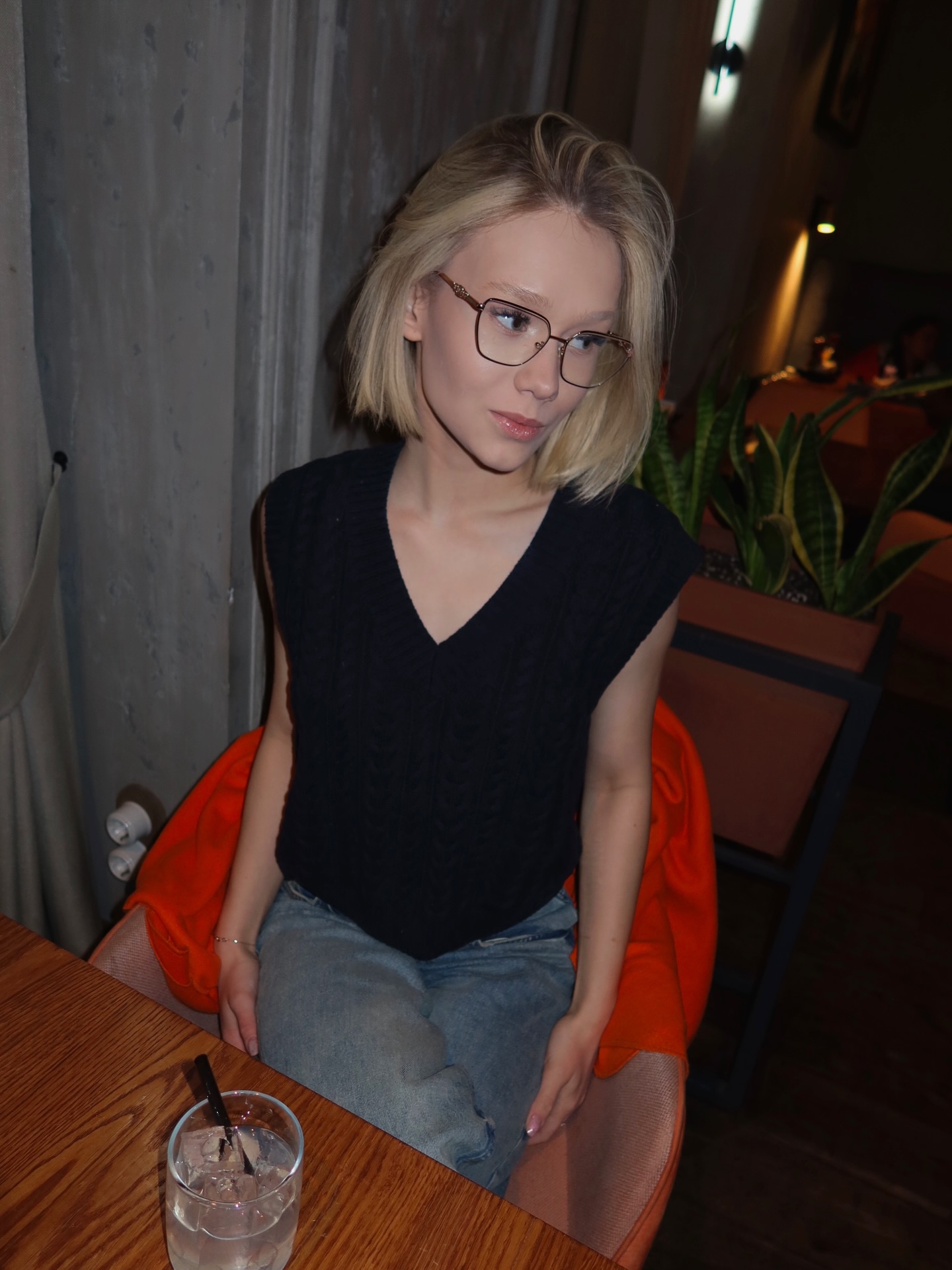 tollysage sitting at a table wearing black sleeveless knit top in restaurant interior