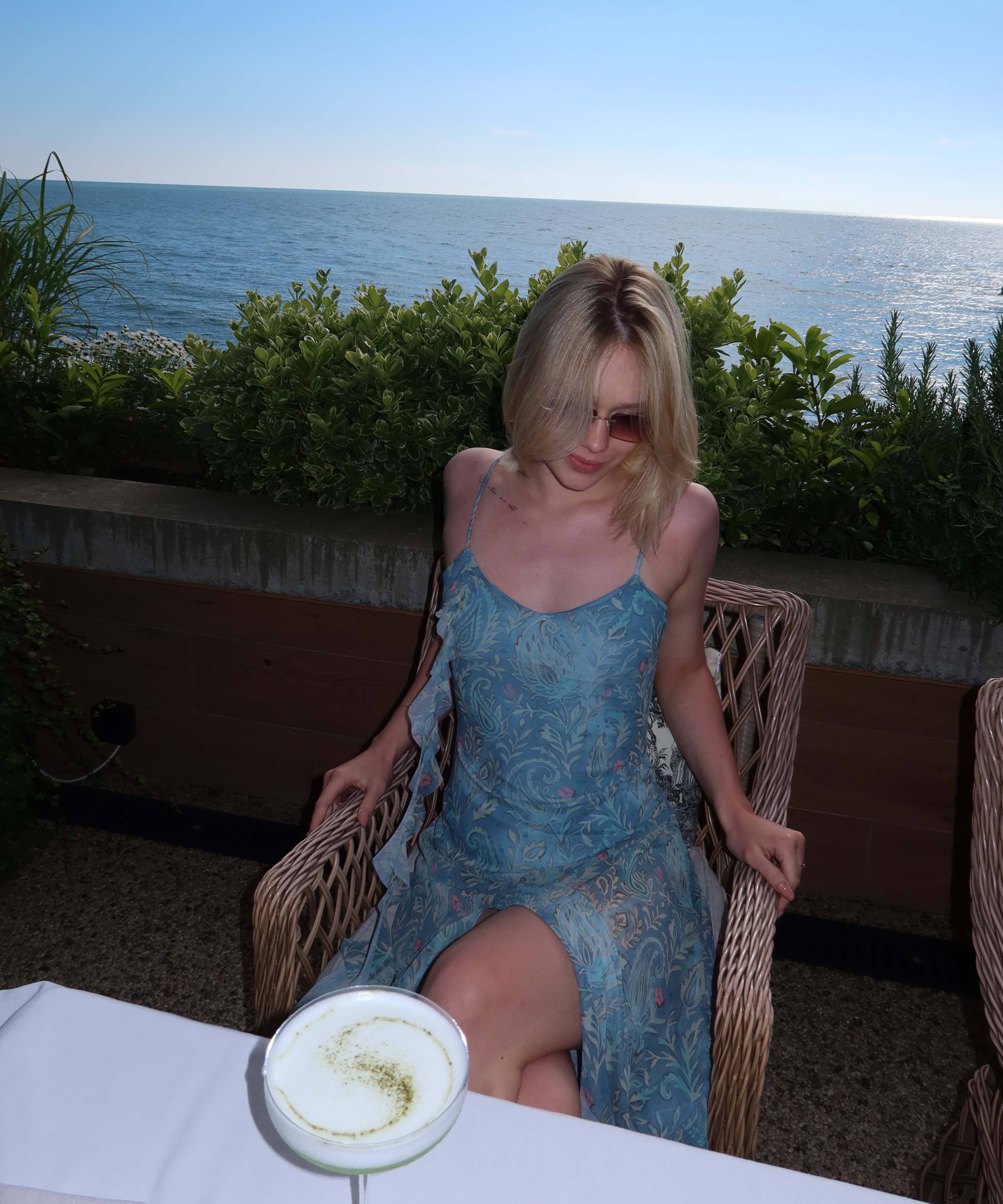 tollysage sitting in a wicker chair wearing blue floral dress in seaside terrace