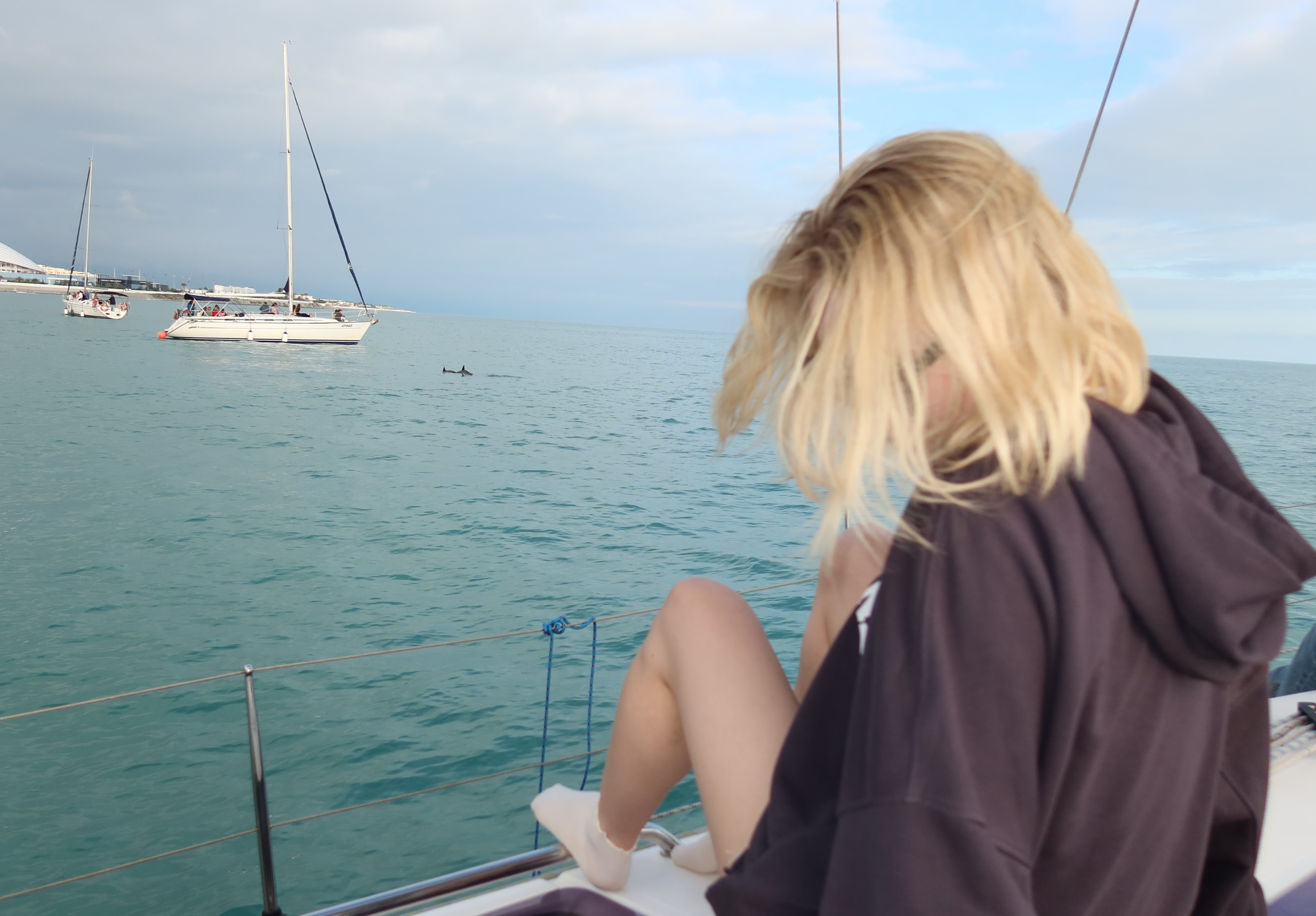 tollysage sitting on boat railing wearing dark brown hoodie in sailboat deck at sea