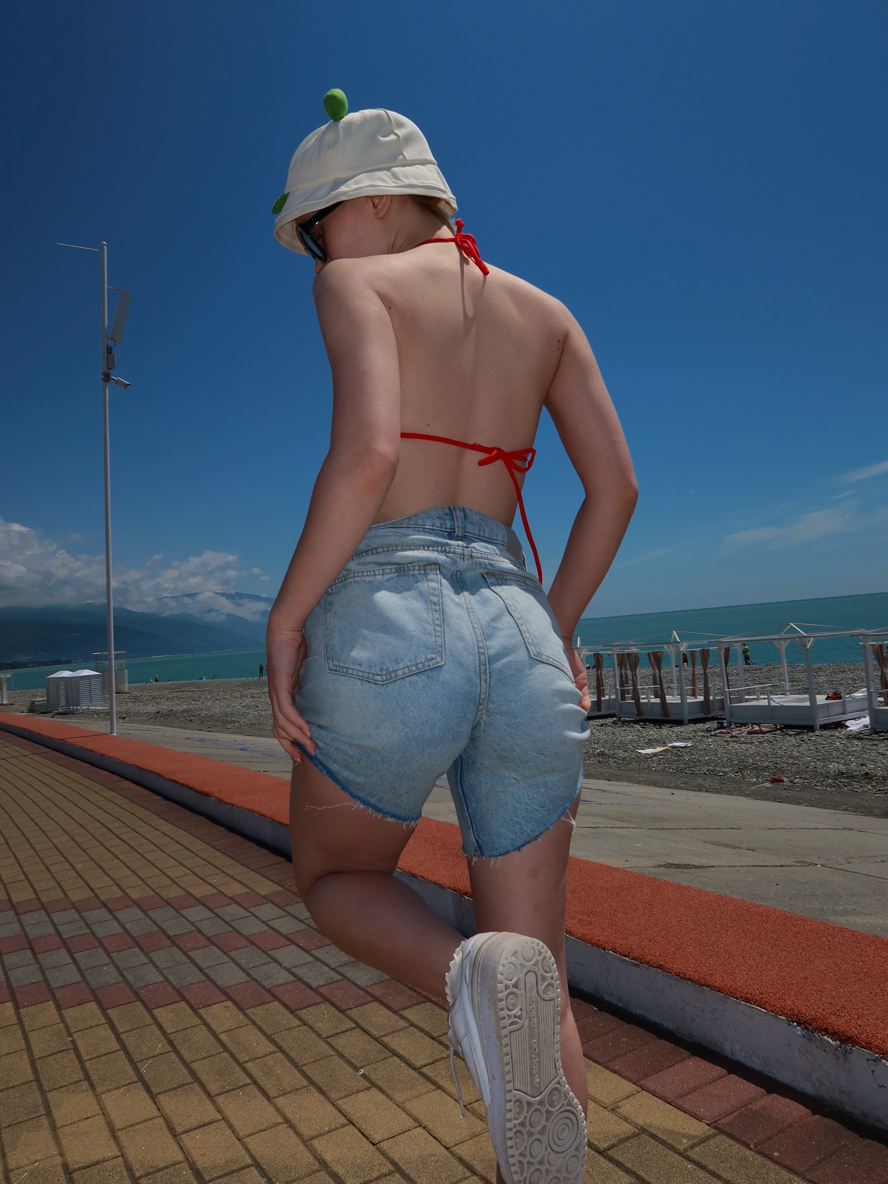 tollysage posing looking back wearing light blue denim shorts in beachfront promenade