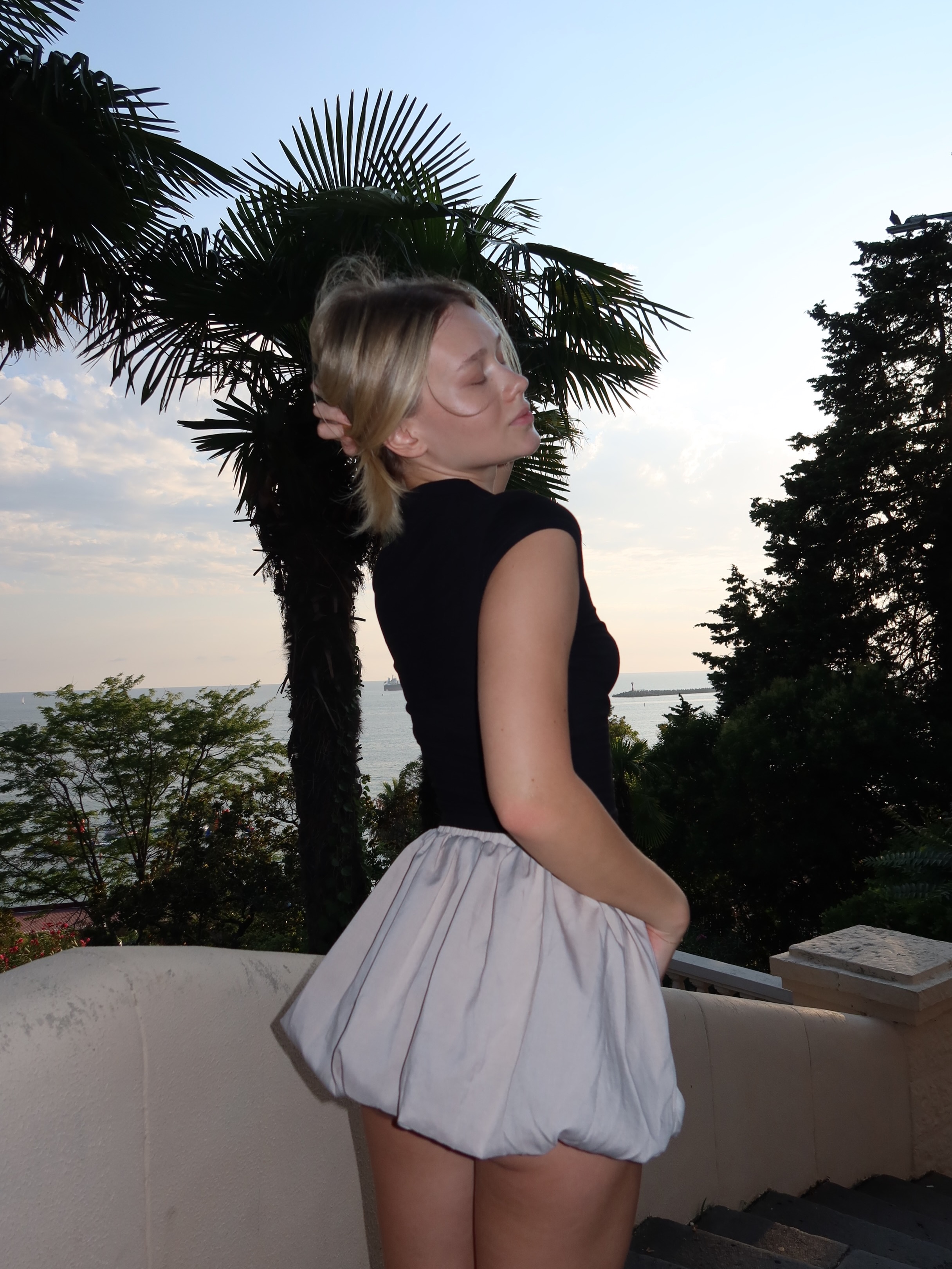 tollysage posing on steps wearing black top in terrace near sea