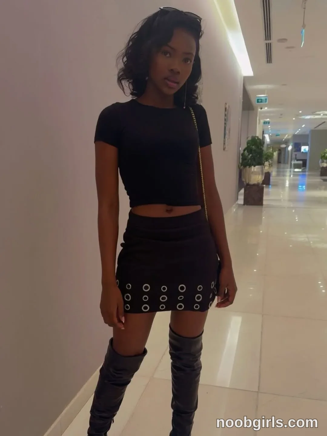tootie03 Standing facing the camera with her arms lowered wearing Black short-sleeved cropped top in corridor