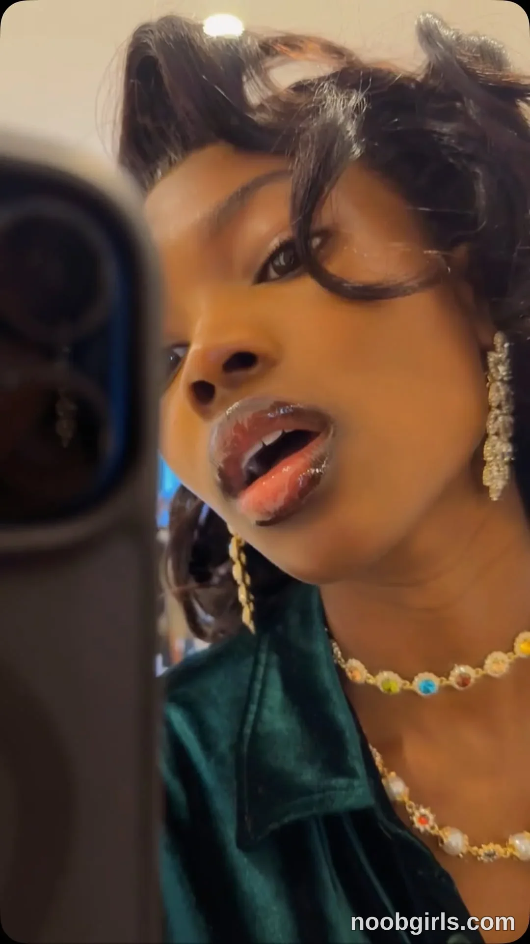 tootie03 Tilting her head with her mouth open beside a smartphone wearing Dark green collared garment