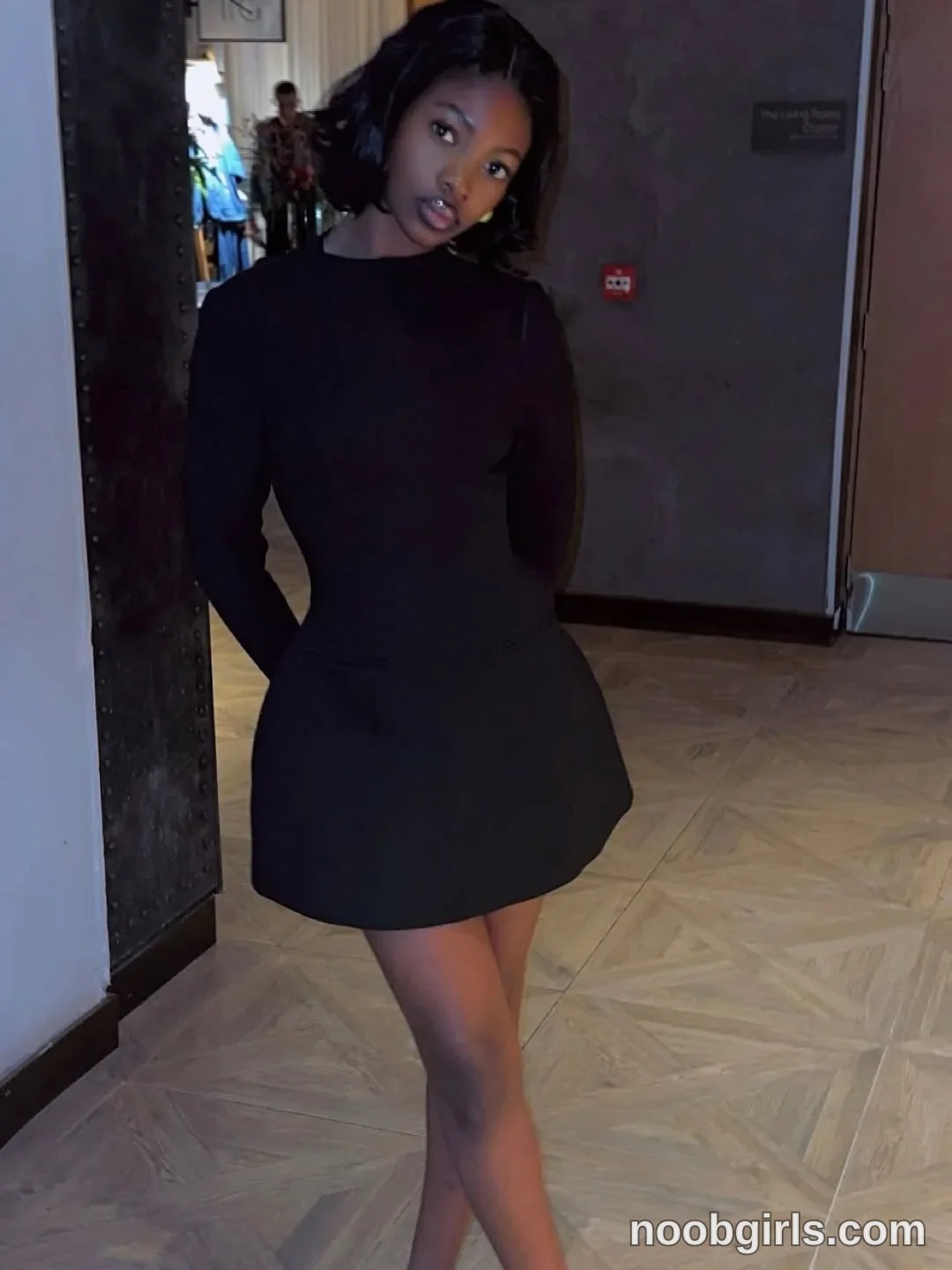 tootie03 Standing with her hands behind her back wearing Black long-sleeved mini dress with a fitted waist and flared skirt