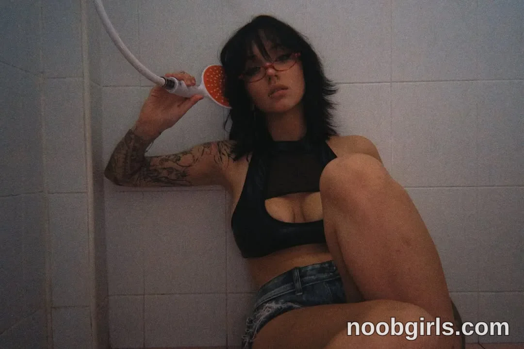 vivian_qwerty Sitting against the tiled wall with one knee raised wearing Black sleeveless cropped top with a chest cutout