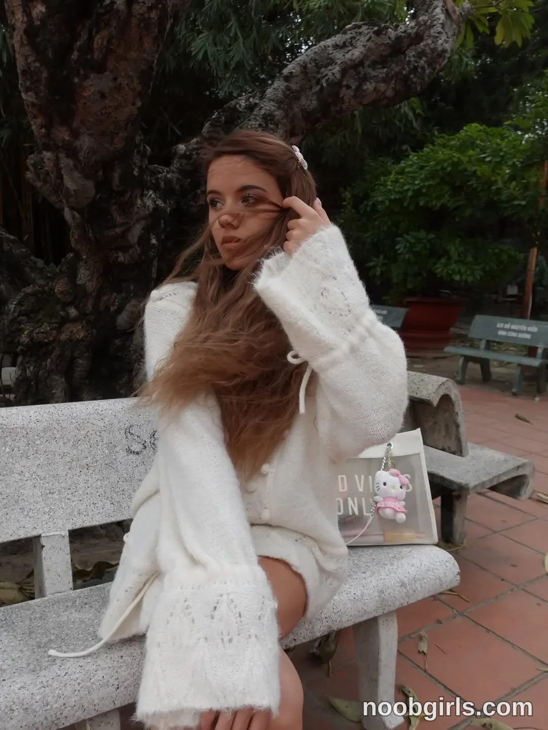 waki_lucky Sitting on a stone bench with one hand raised to her hair beside her face