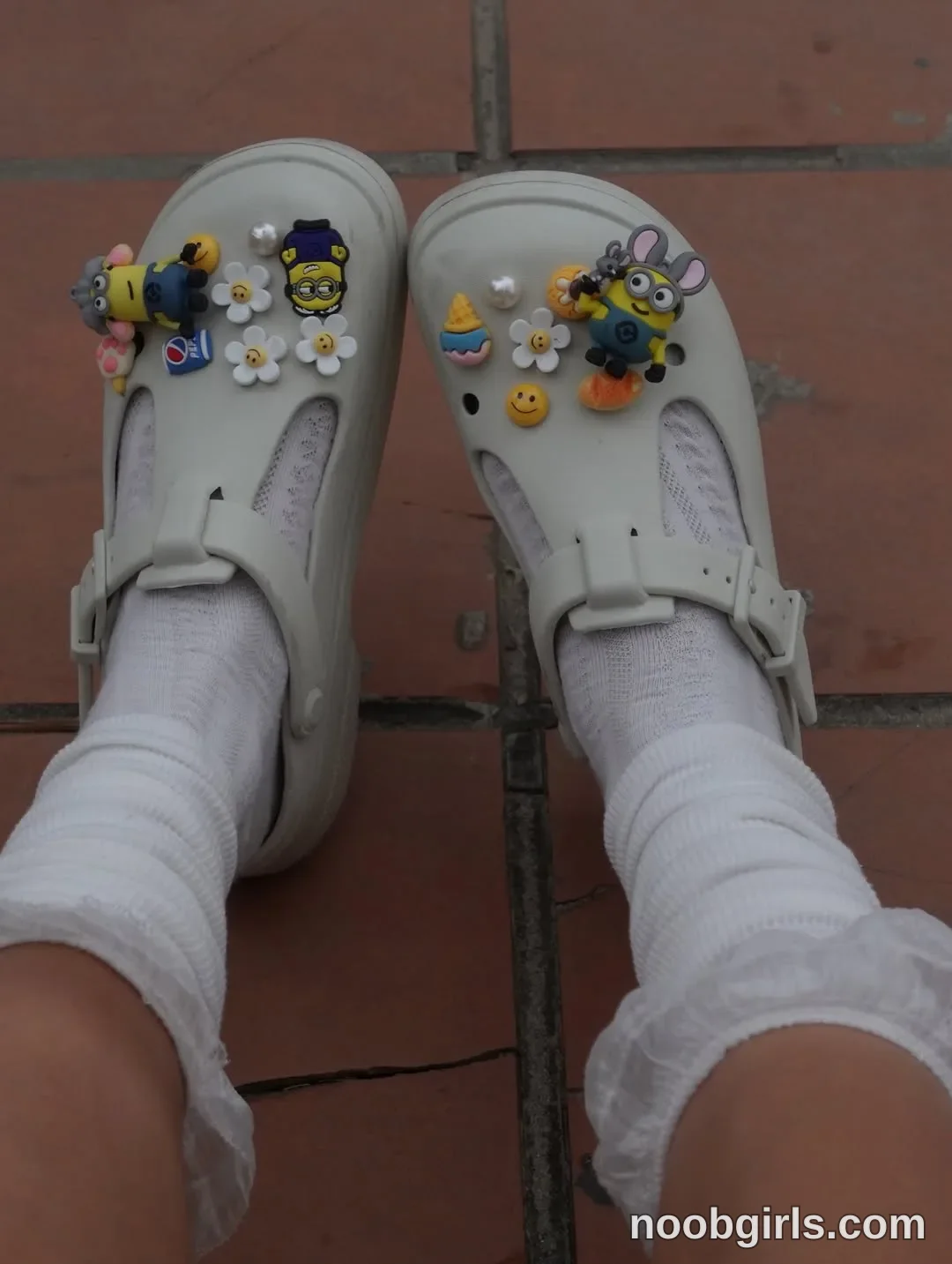 waki_lucky Her feet are resting on the tiled floor wearing Light grey clogs with heel straps and colourful decorative charms