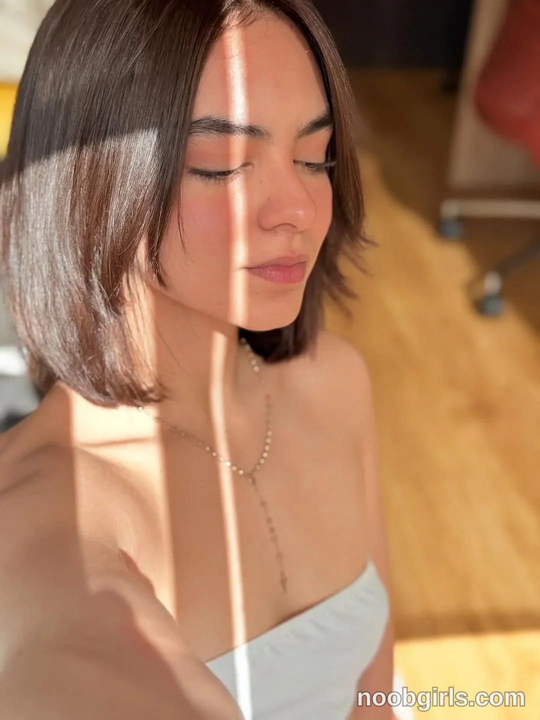 Wale looking downwards with eyes cast down or closed wearing white strapless tube top in room