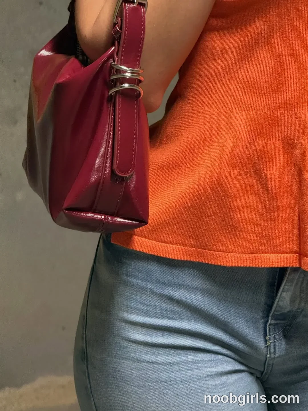 Wale standing with a shoulder bag held under the arm wearing orange short-sleeved knit top