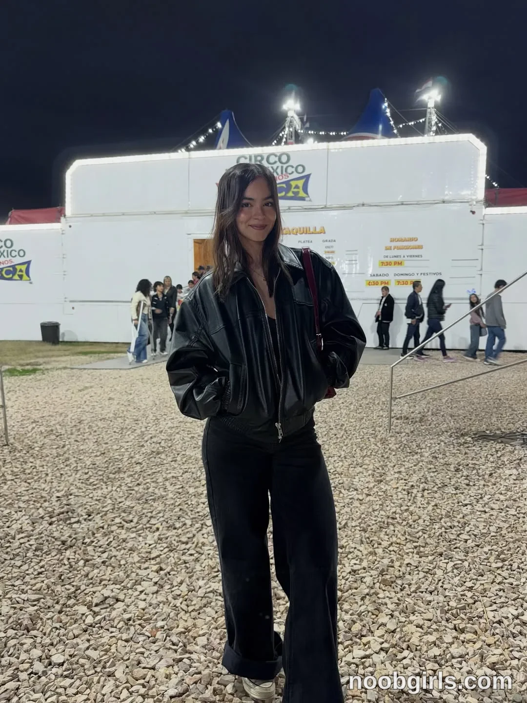 Wale wearing black leather bomber-style jacket in fairground or circus grounds in front of a white ticket booth trailer