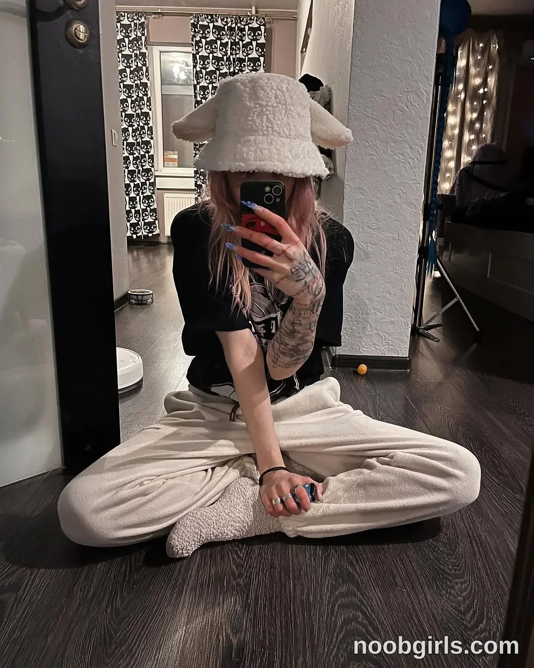 Lina Seated cross-legged on the floor wearing off-white plush hat with floppy ear-like sides in residential room or hallway
