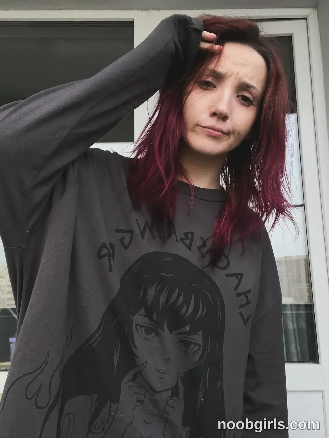 Lina holding the top of her head wearing dark gray long-sleeved shirt with a black printed graphic in front of a building